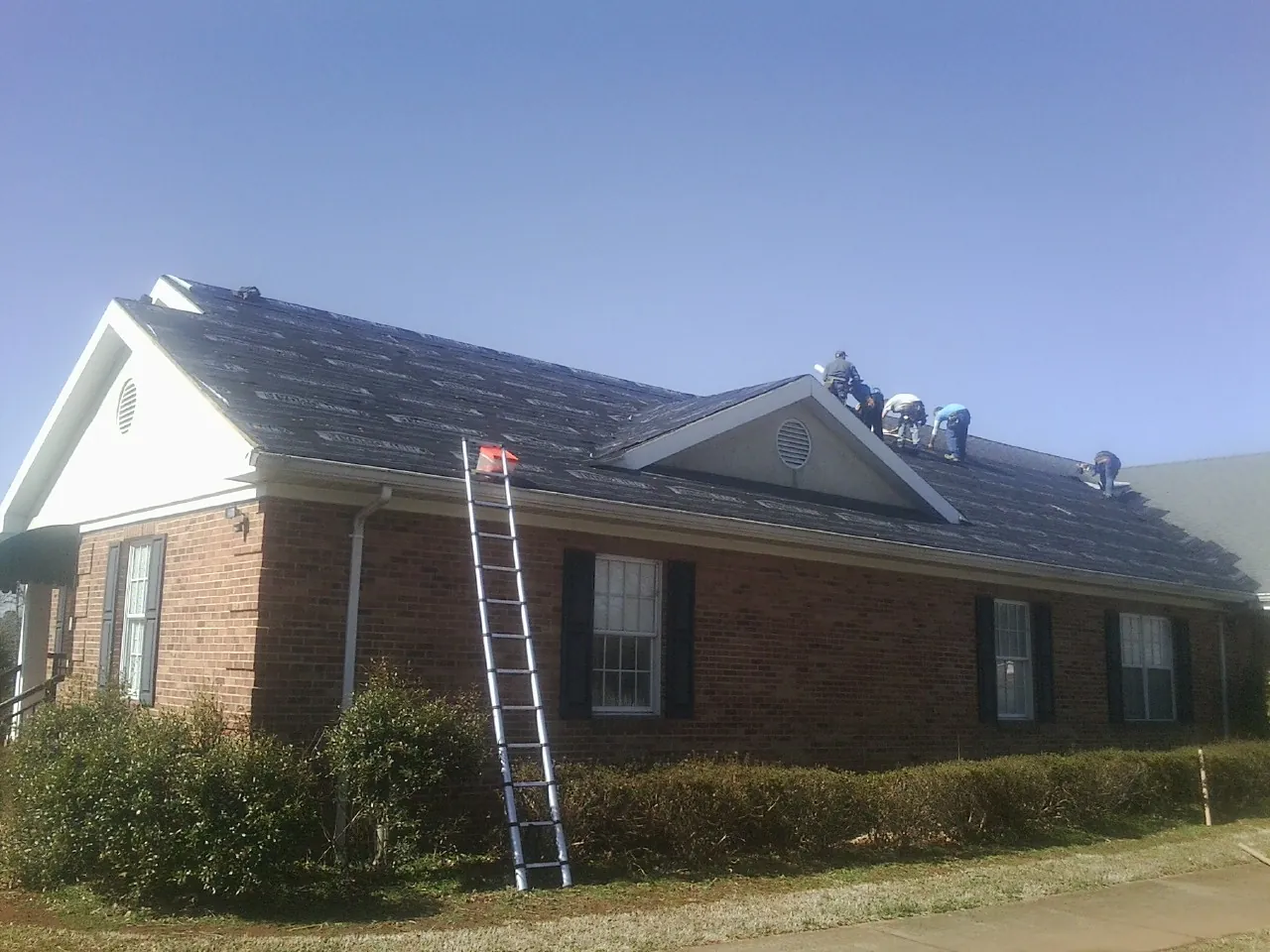 Crew tearing shingles off a brick ranch roof with a ladder set — Emergency Roof Repair work by our crew in Kittery