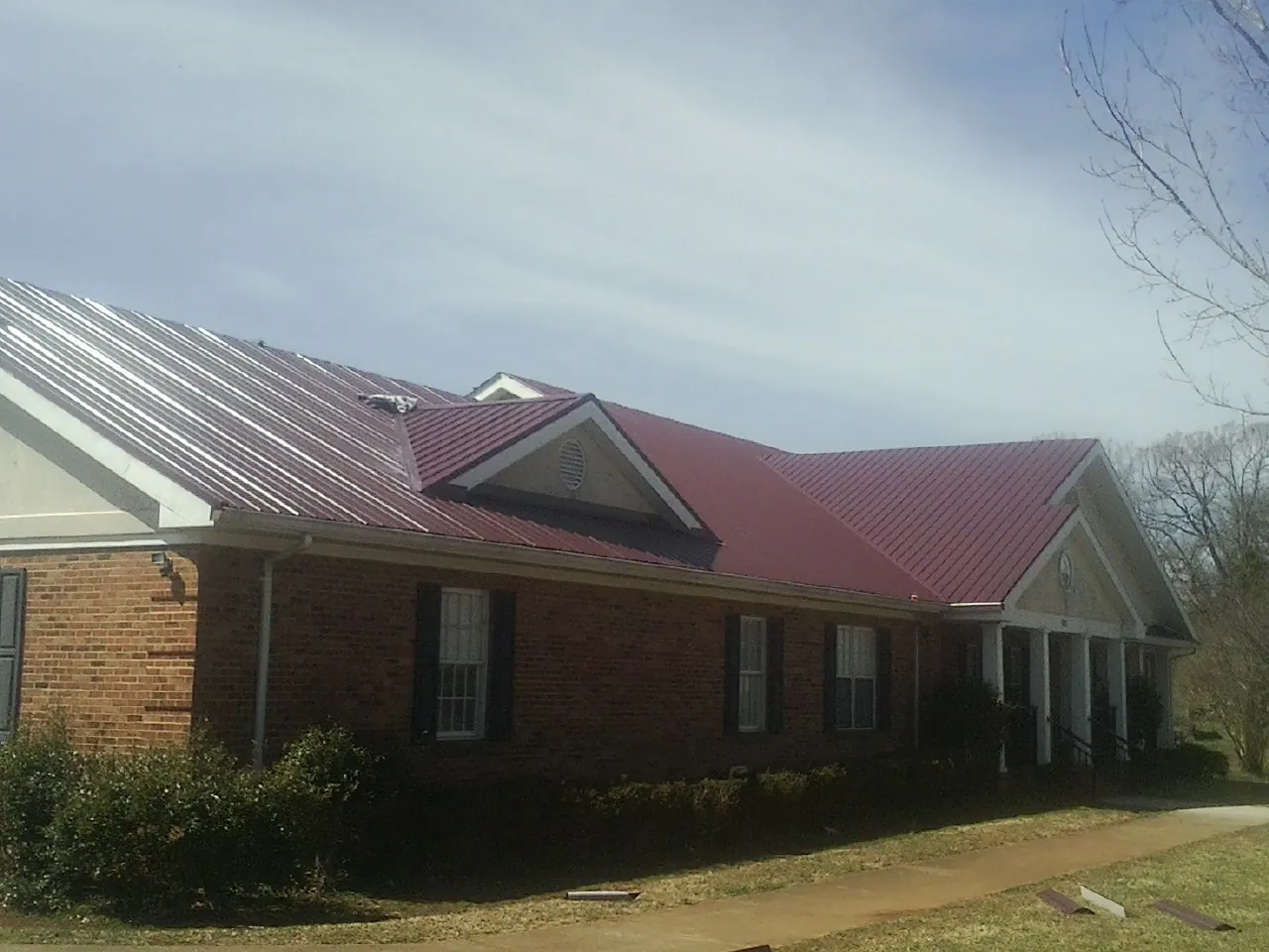 Red metal roof with gabled entries on a long brick building, from a Hail Damage Roof Repair job in Kittery