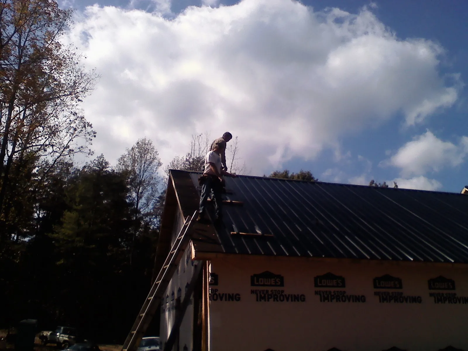 Roofer fastening dark metal panels high against a cloudy sky, from a Roof Inspection job in Kittery