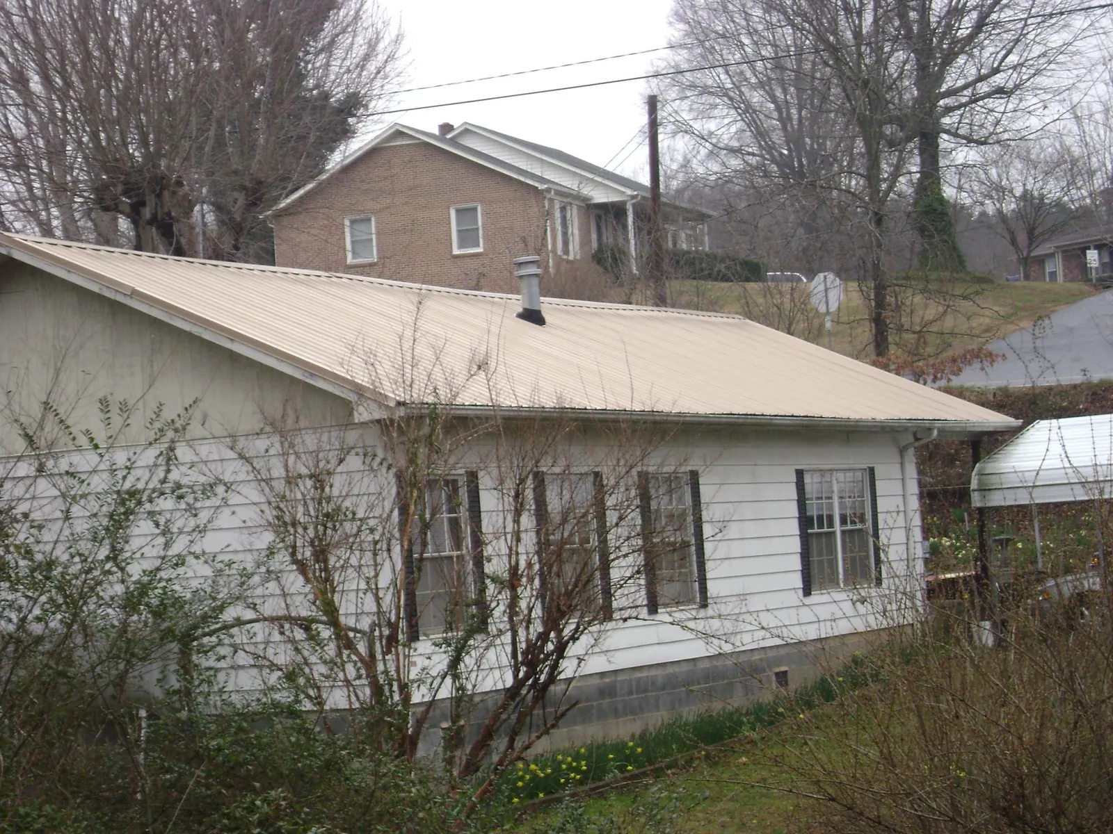Tan metal roof on a white sided house set into a hillside — Commercial Roofing by Roofing Brothers in Kittery